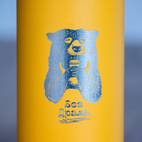 graviran-termos-za-planina Close-up of laser-engraved bear holding a cup with the text “Bez drama” on a yellow metal thermos.