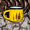 kanche-malko-za-kafe Yellow enamel mug with black rim and illustration of a campfire, tent, and pine trees with the text “Don’t burn the forest, light the fire in your soul”, photographed outdoors on bark.