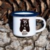 White enamel mug with blue rim and black bear illustration holding a cup with the text “No Drama”, placed outdoors on bark.