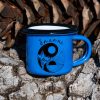 Small blue enamel mug with yin-yang mountain and sun illustration and text “Balance”, placed outdoors on bark.