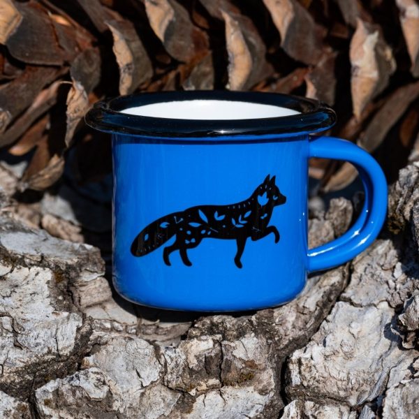 Small blue enamel mug with black running fox illustration, placed outdoors on bark.