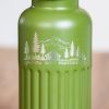 Close-up of laser-engraved mountain and cabin design on a green metal bottle.