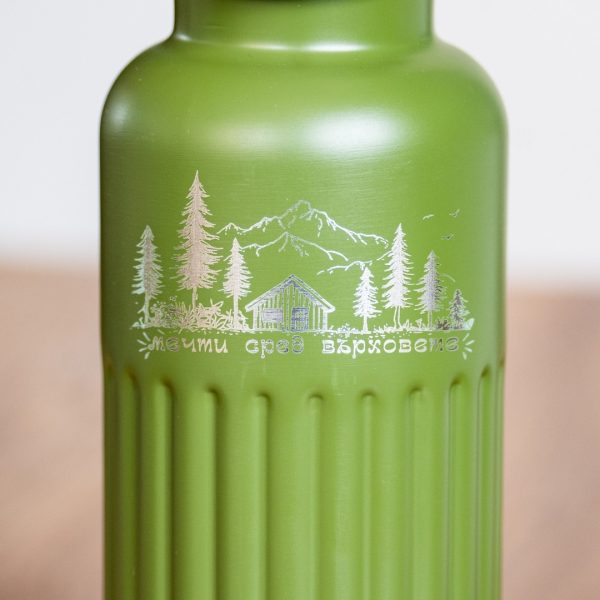 Close-up of laser-engraved mountain and cabin design on a green metal bottle.