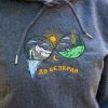 broderia-do-bezkraya-varhu-tumnosiv-suitshart-s-kachulka Close-up of colourful embroidered mountain landscape with “До безкрая” text on a dark grey hoodie