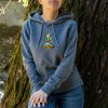 tumnosiv-uniseks-suitshart-s-kachulka-i-broderia-meowtain-climber-za-zhena Woman wearing a dark grey unisex hoodie with embroidered “Meowtain Climber” cat mountain design outdoors