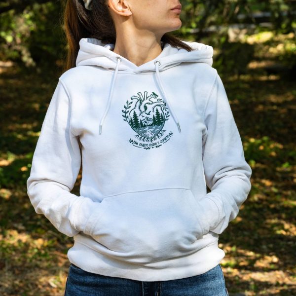 byal-uniseks-suitshart-s-kachulka-i-broderia-sartse-za-zhena Woman wearing a white unisex hoodie with embroidered anatomical heart and mountain landscape design outdoors