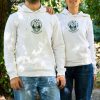 byal-uniseks-suitshart-s-kachulka-i-broderia-sartse Two people wearing white unisex hoodies with embroidered anatomical heart and mountain landscape design outdoors