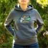 tumnosiv-uniseks-suitshart-s-kachulka-i-broderia-do-bezkraya-za-zhena Woman wearing a dark grey unisex hoodie with embroidered mountain landscape and “До безкрая” design outdoors